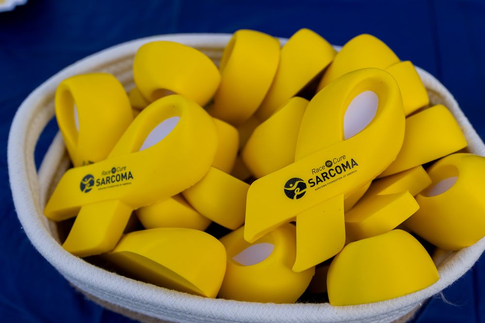 Basket of yellow sarcoma awareness ribbon-shaped stress toys with Sarcoma logo imprint at charity event.