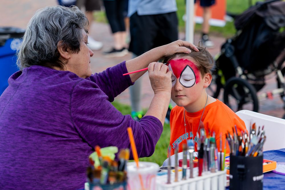 Face painter applying Spiderman design on a child's face at an outdoor festival event.