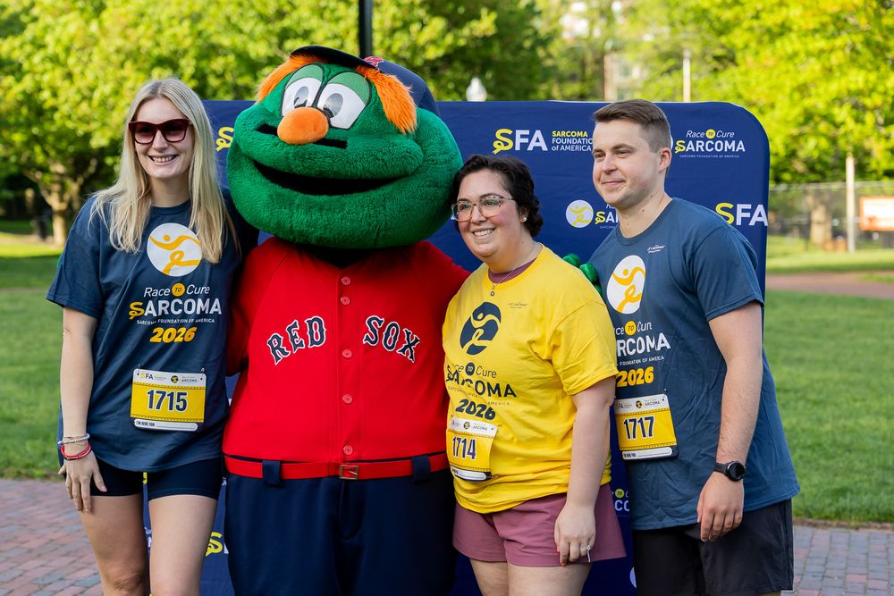 Group posing with Wally the Green Monster mascot at SFA Sarcoma charity fundraising event outdoors.