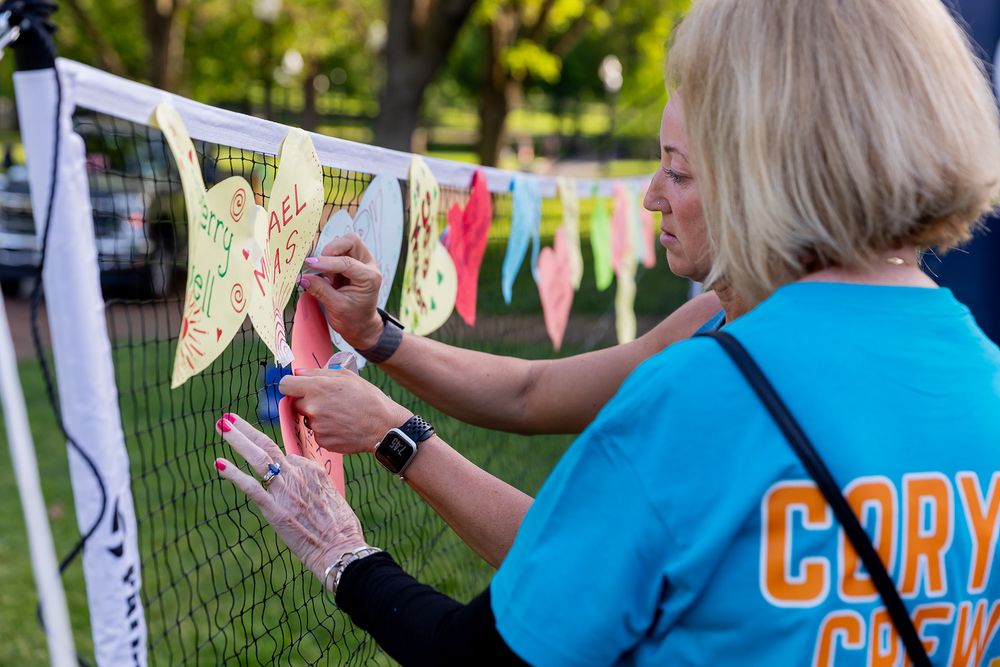 Woman in blue Cory Crew shirt attaching colorful butterfly decorations to an outdoor net display.
