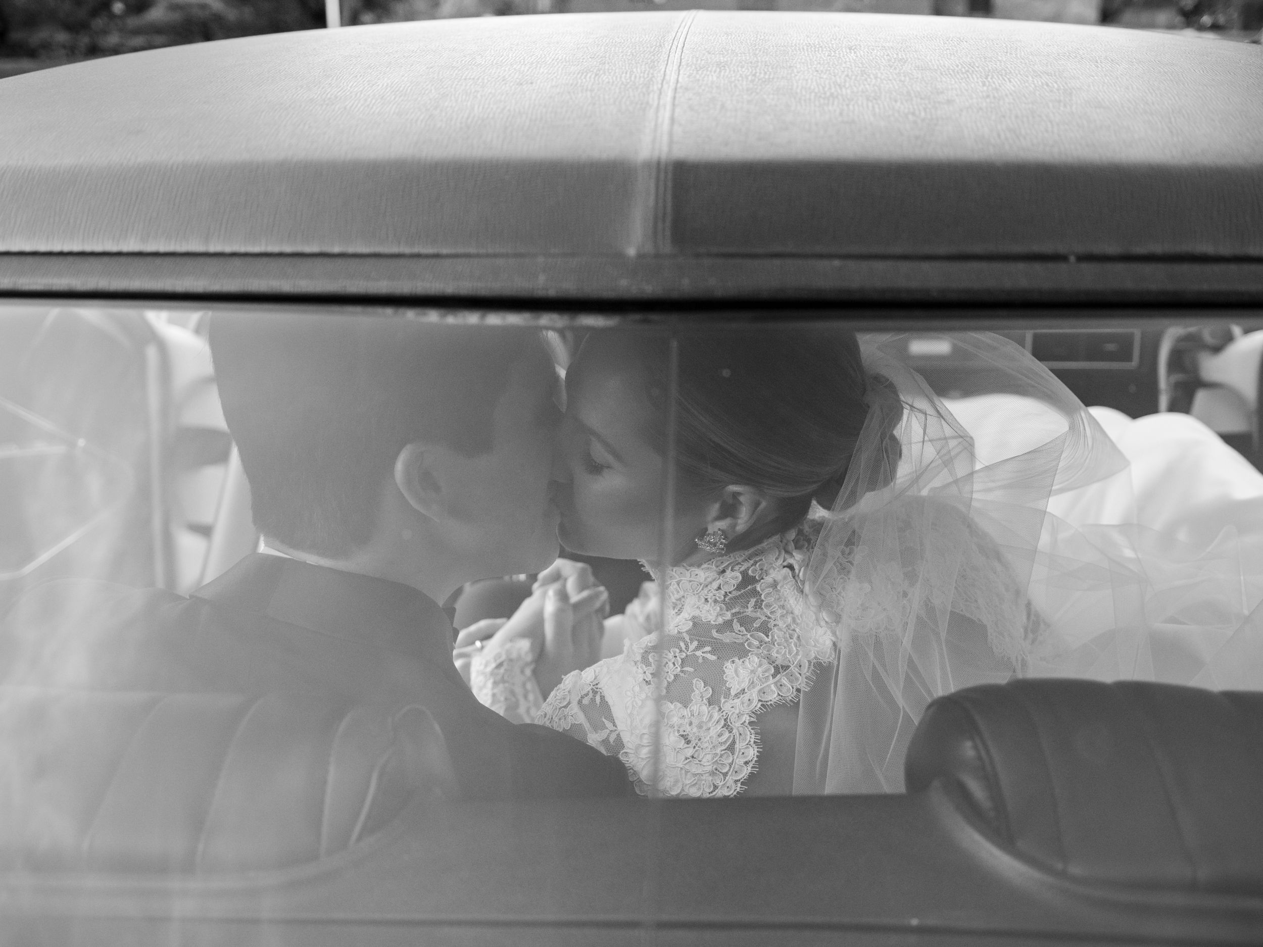 Black and white view through car window showing delicate white lace veil fabric against dark interior.