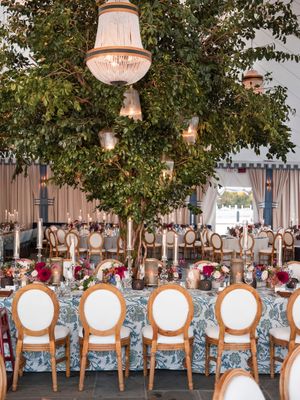 Elegant wedding reception setup with crystal chandeliers and white chairs arranged in front of floral-decorated dining tables.
