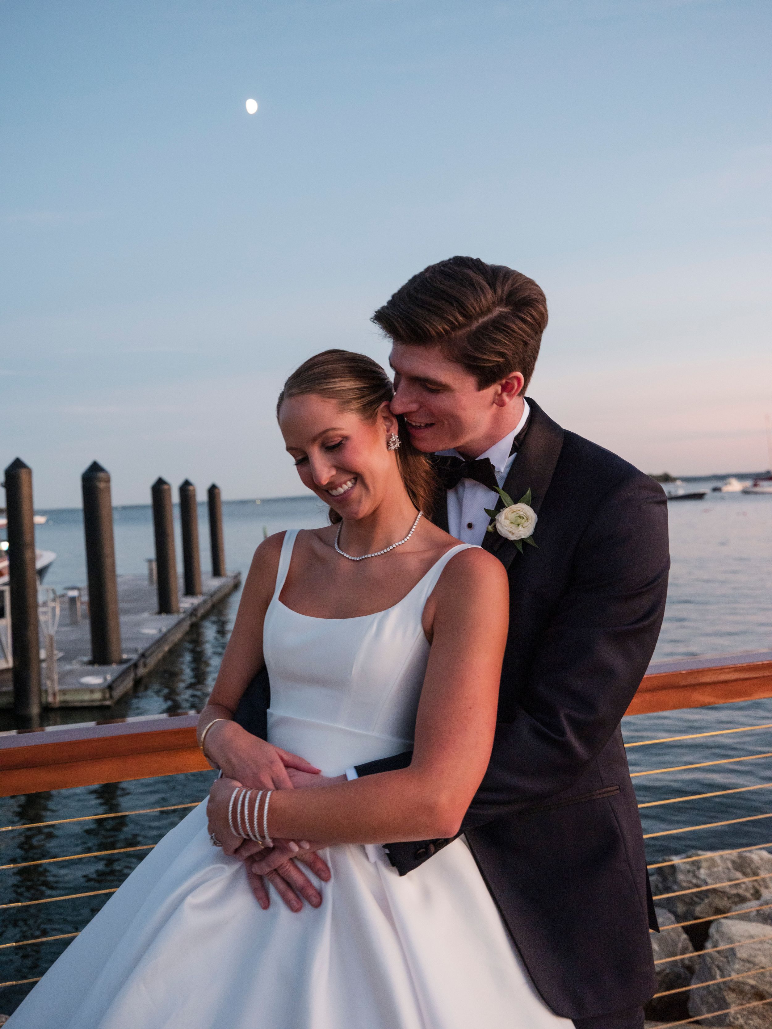 A romantic couple shares tender moments on a wooden dock by the water at sunset.