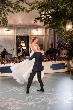 A couple performs an elegant dip during their first dance on a white dance floor with decorative patterns.