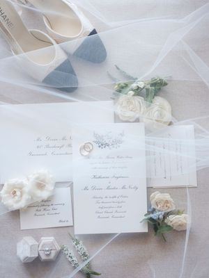 Elegant wedding stationery and invitations displayed with white roses and delicate floral accents on a light background.