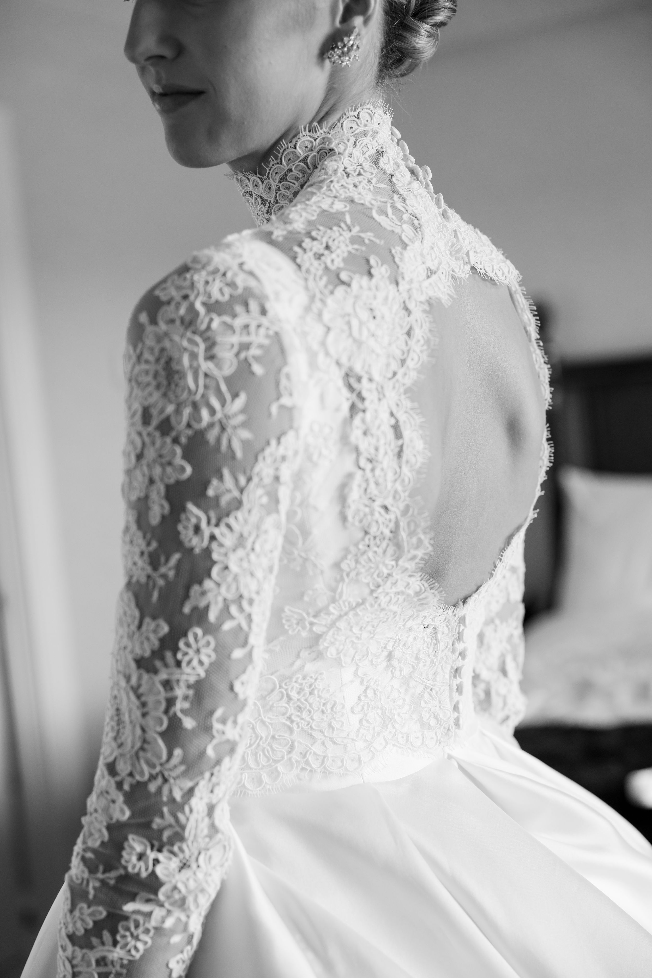 Close-up black and white photo of intricate lace details on back of wedding dress with long sleeves and high neckline.