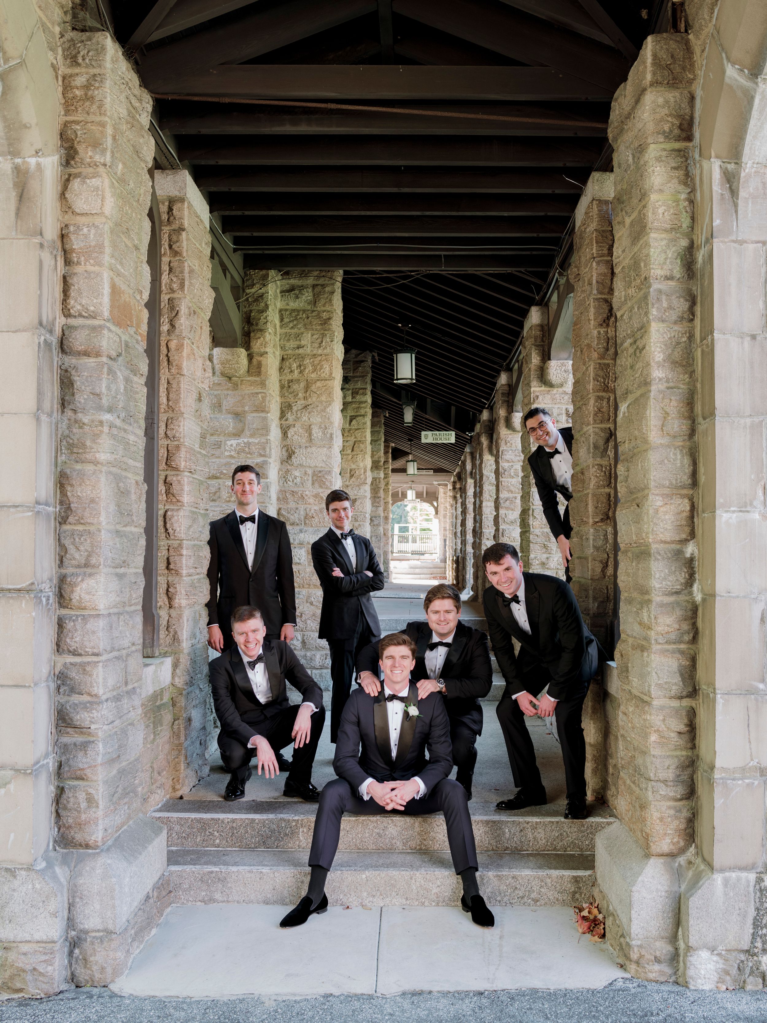 Wedding party poses playfully in stone archways of historic building, creating fun panoramic sequence.