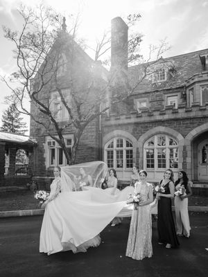 Wedding party performs a choreographed dance routine on the lawn of a historic stone building with arched windows.