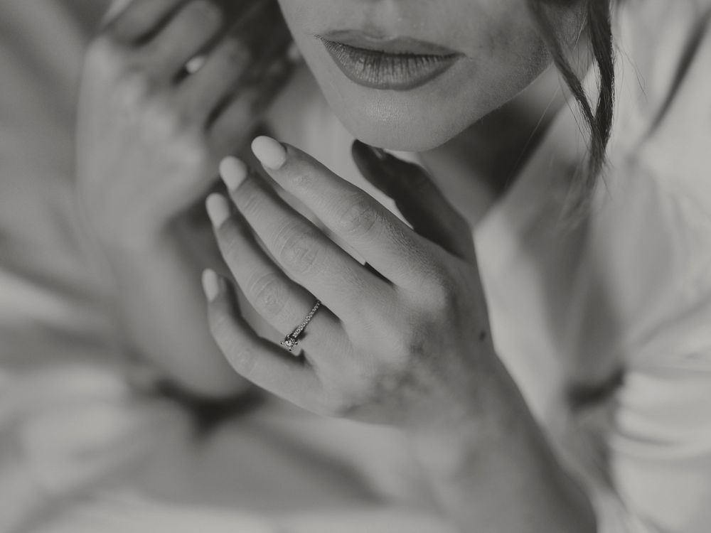 Black and white close-up of a bride resting her hands near her face showcasing her engagement ring.