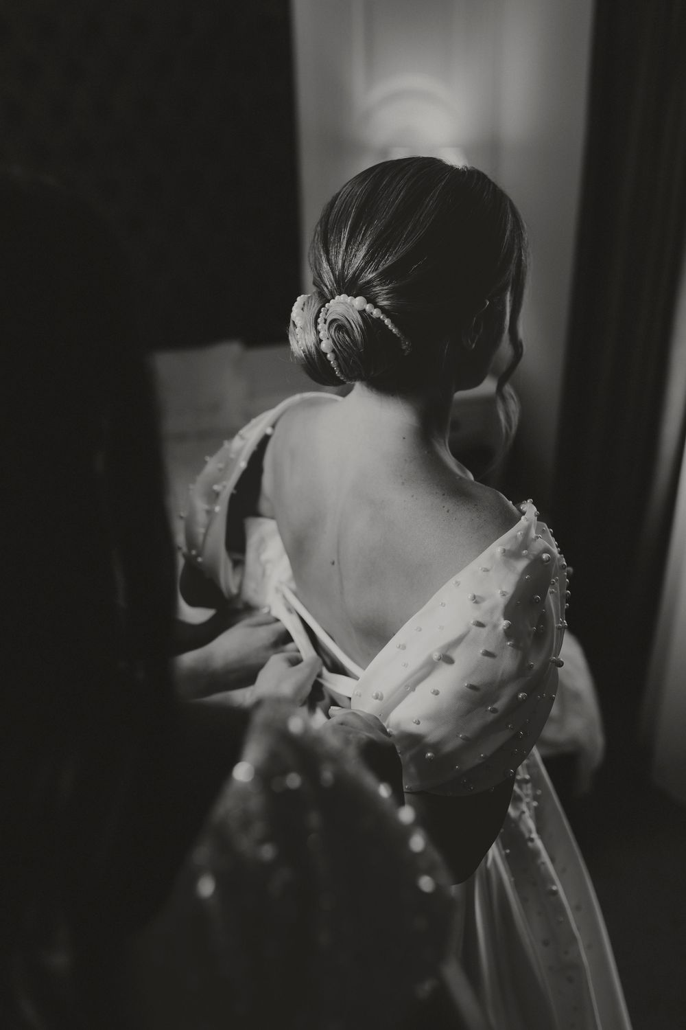 Black and white photo of bride in backless pearl wedding gown with elegant updo hair accessory.