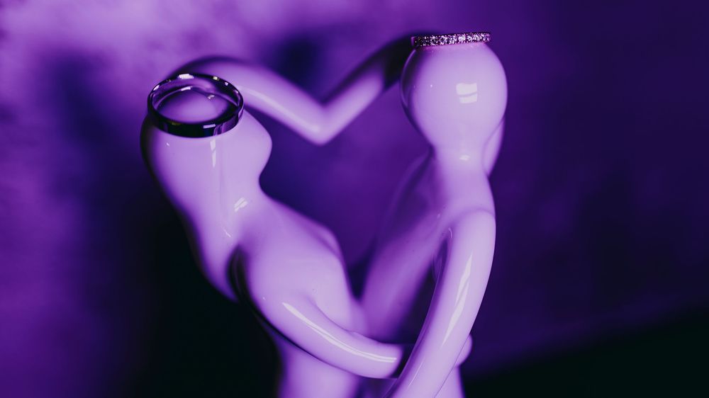Wedding rings displayed on purple-lit dancing couple figurine in romantic close-up shot.