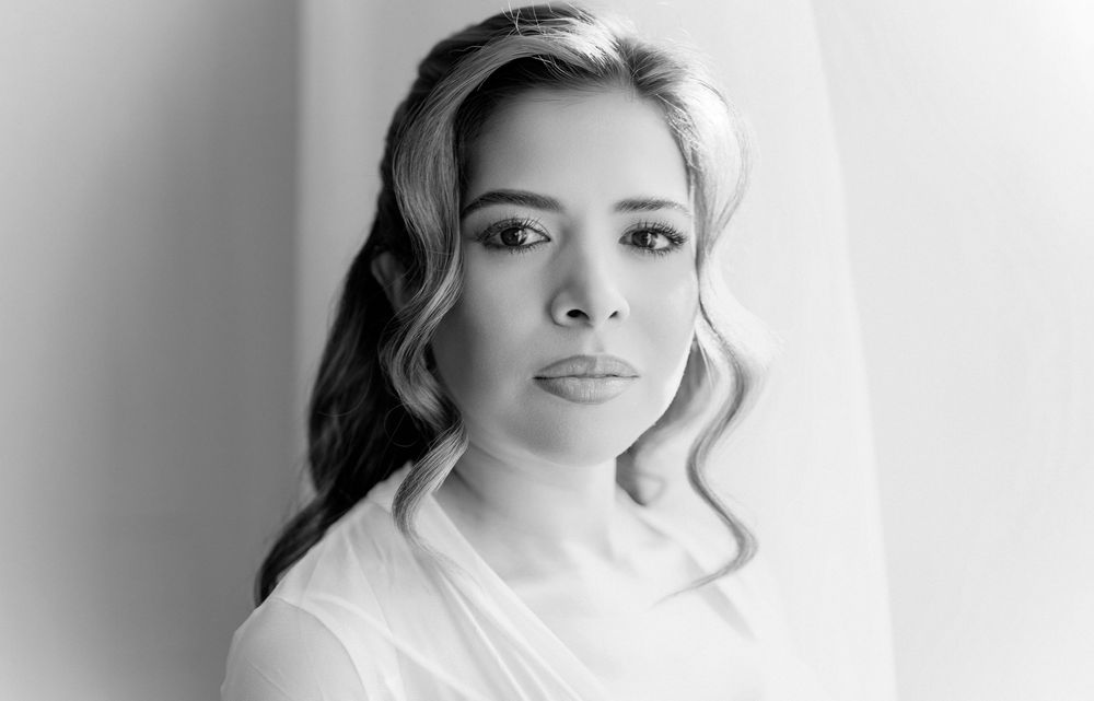 Black and white portrait of a confident woman with wavy hair wearing a white top, studio photography.