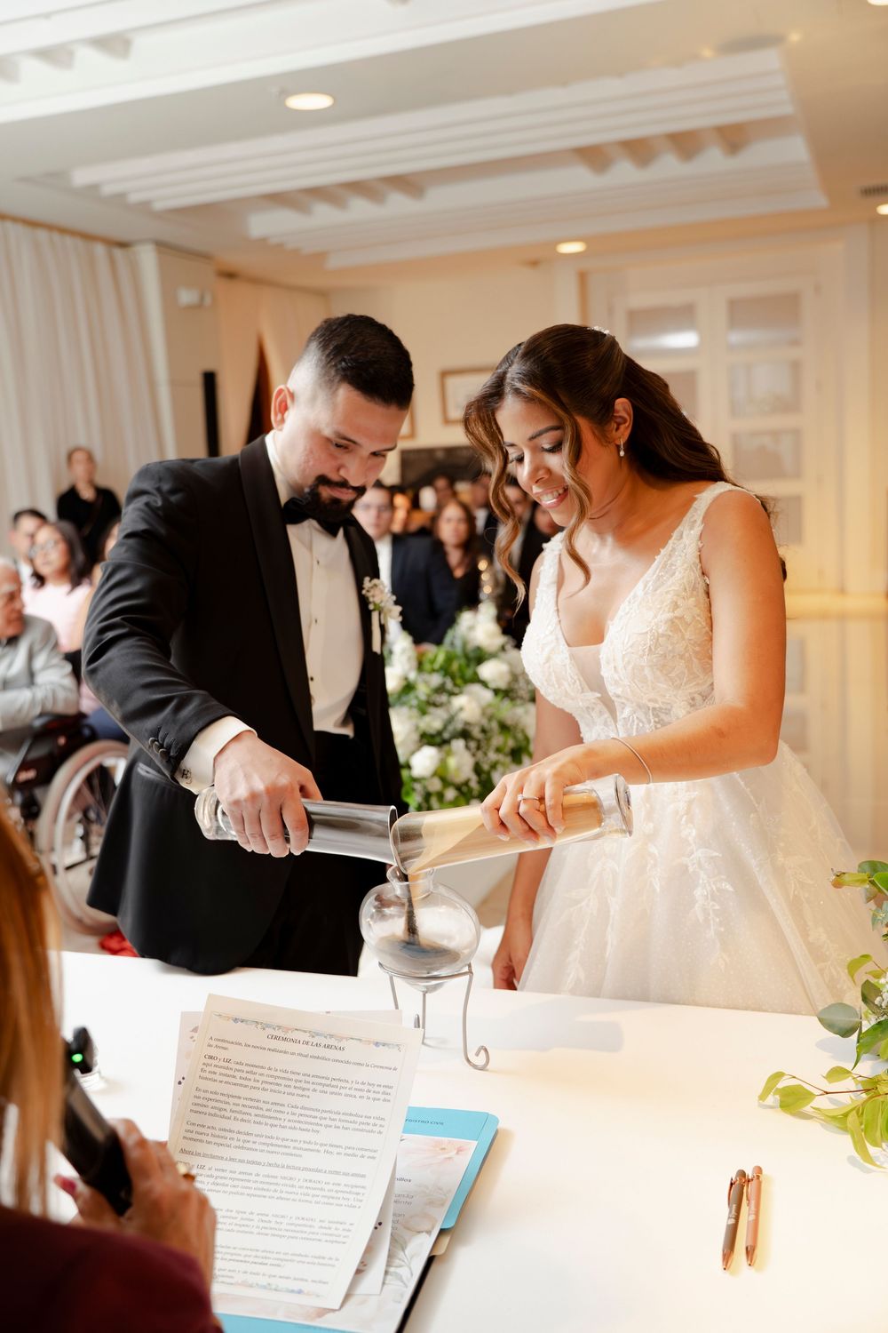 Bride and groom performing sand unity ceremony at wedding reception table.