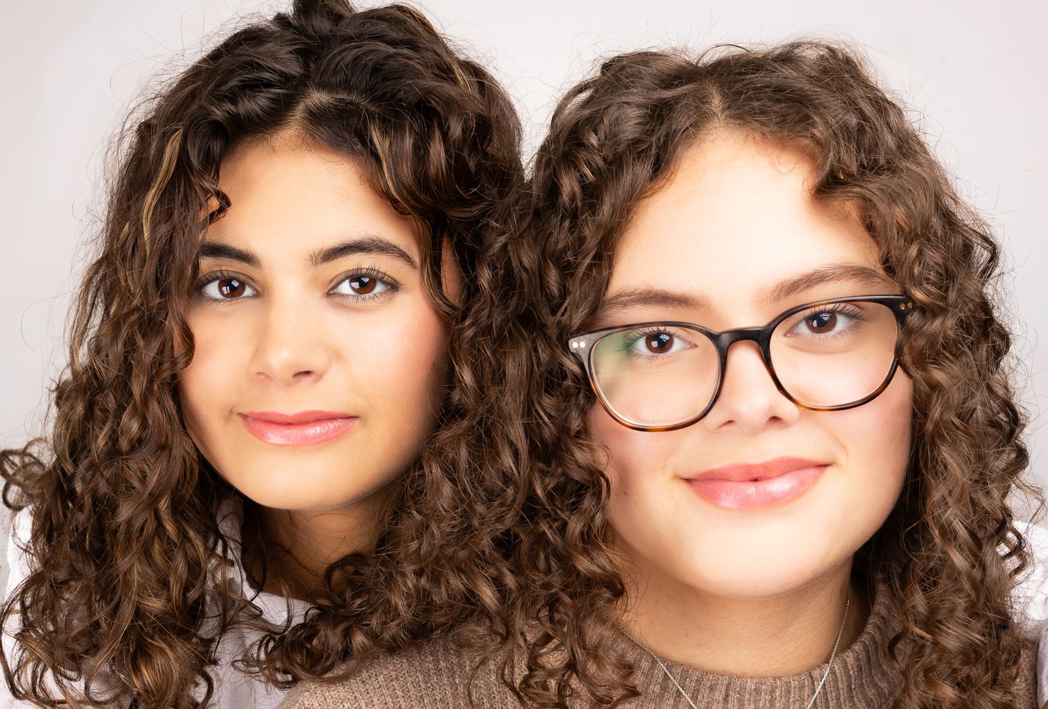 Close-up image of two girls in front of a white/grey backdrop, smiling.