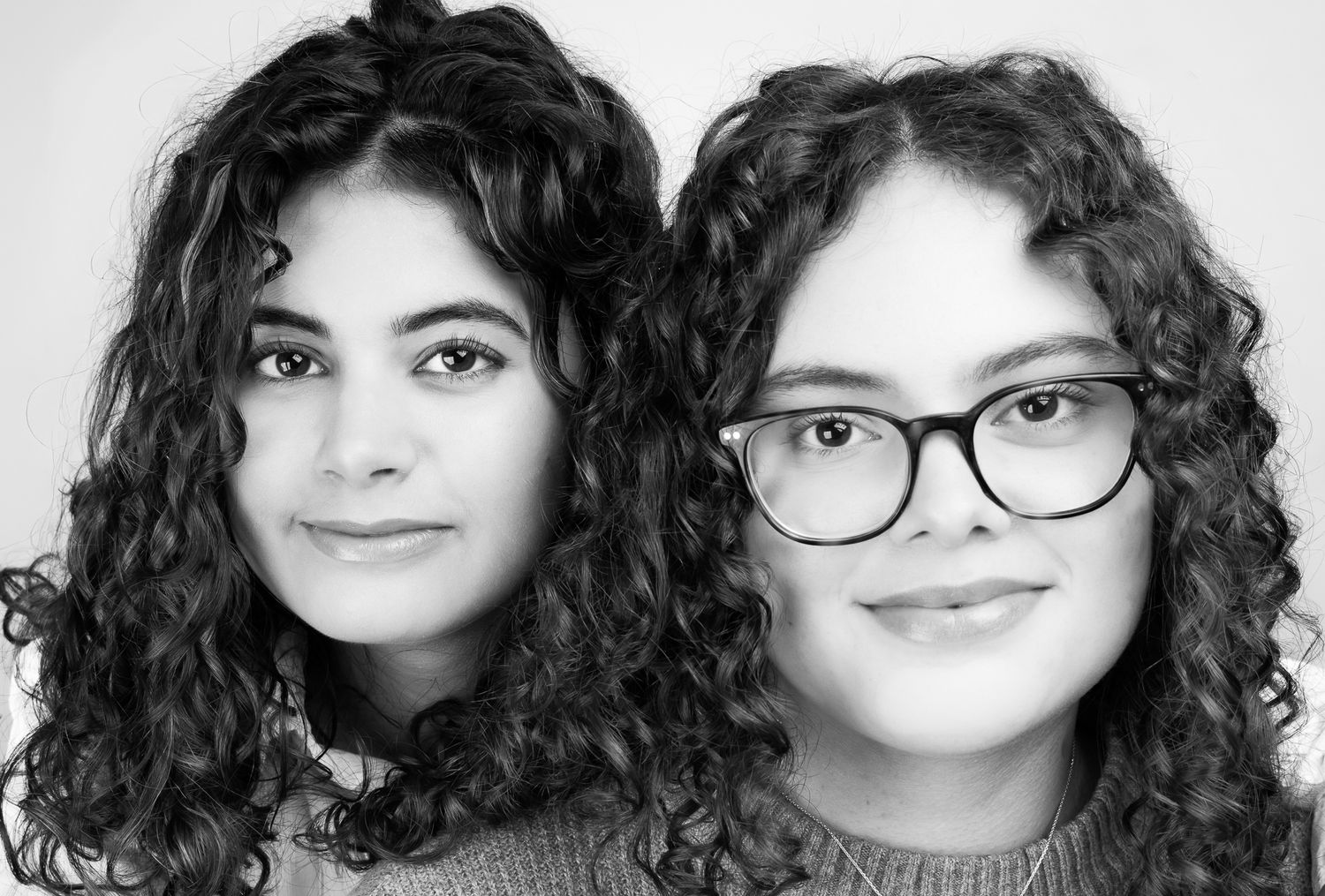 Close-up black and white image of two girls in front of a white/grey backdrop, smiling.