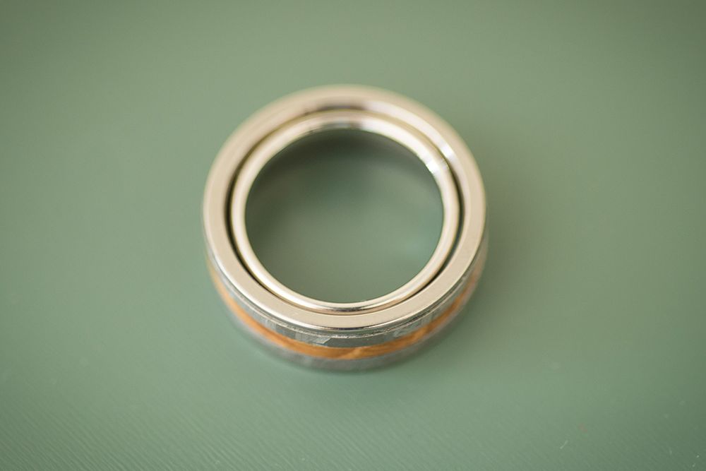 A sleek metal ball bearing with an orange seal is centered on a soft green surface. Two wedding rings one, inside the other.