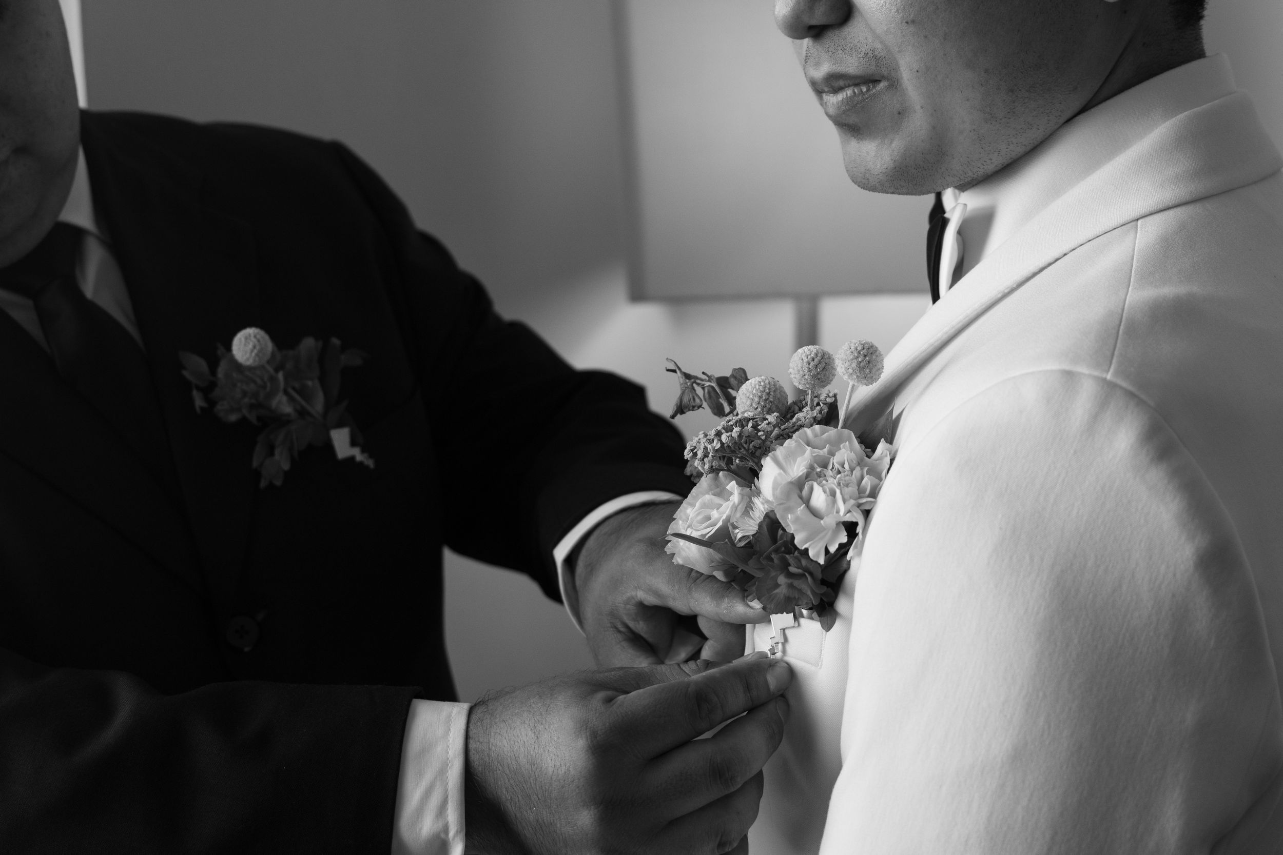 Groom having boutonniere pinned to lapel in black and white wedding photo.