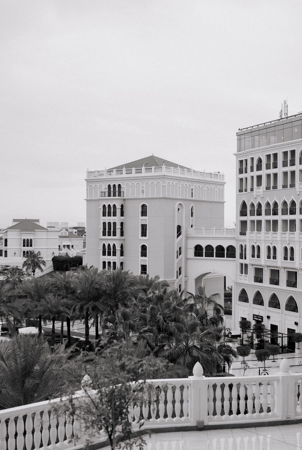 Black and white aerial view of elegant Middle Eastern architecture with arched windows, surrounded by palm trees.