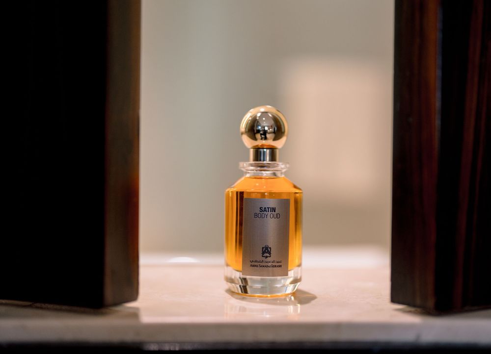 Elegant glass perfume bottle with gold spherical cap containing amber fragrance, displayed on marble shelf in soft light.