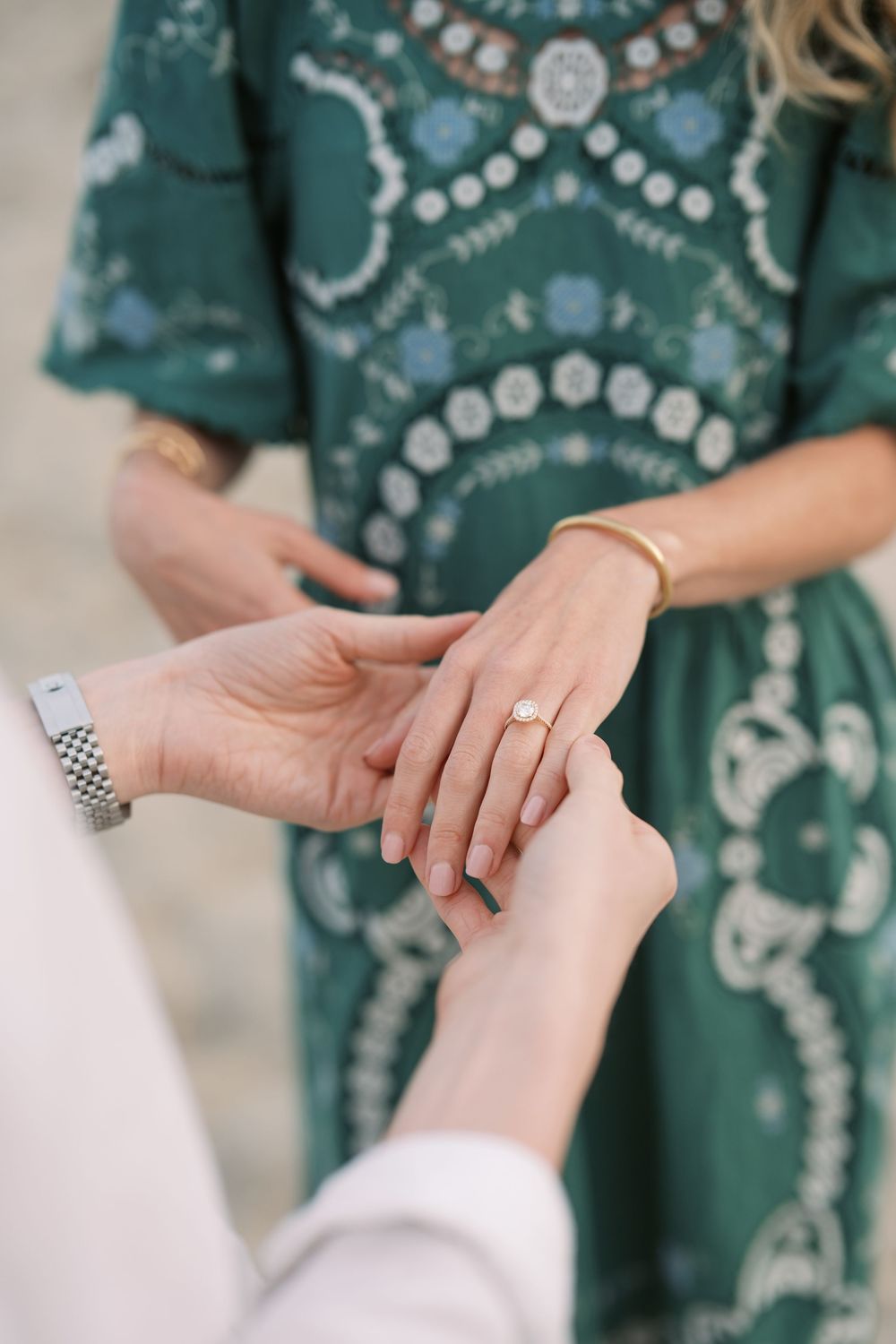 Close-up of a marriage proposal, man placing a diamond engagement ring on womans finger, wearing a green boho dress.