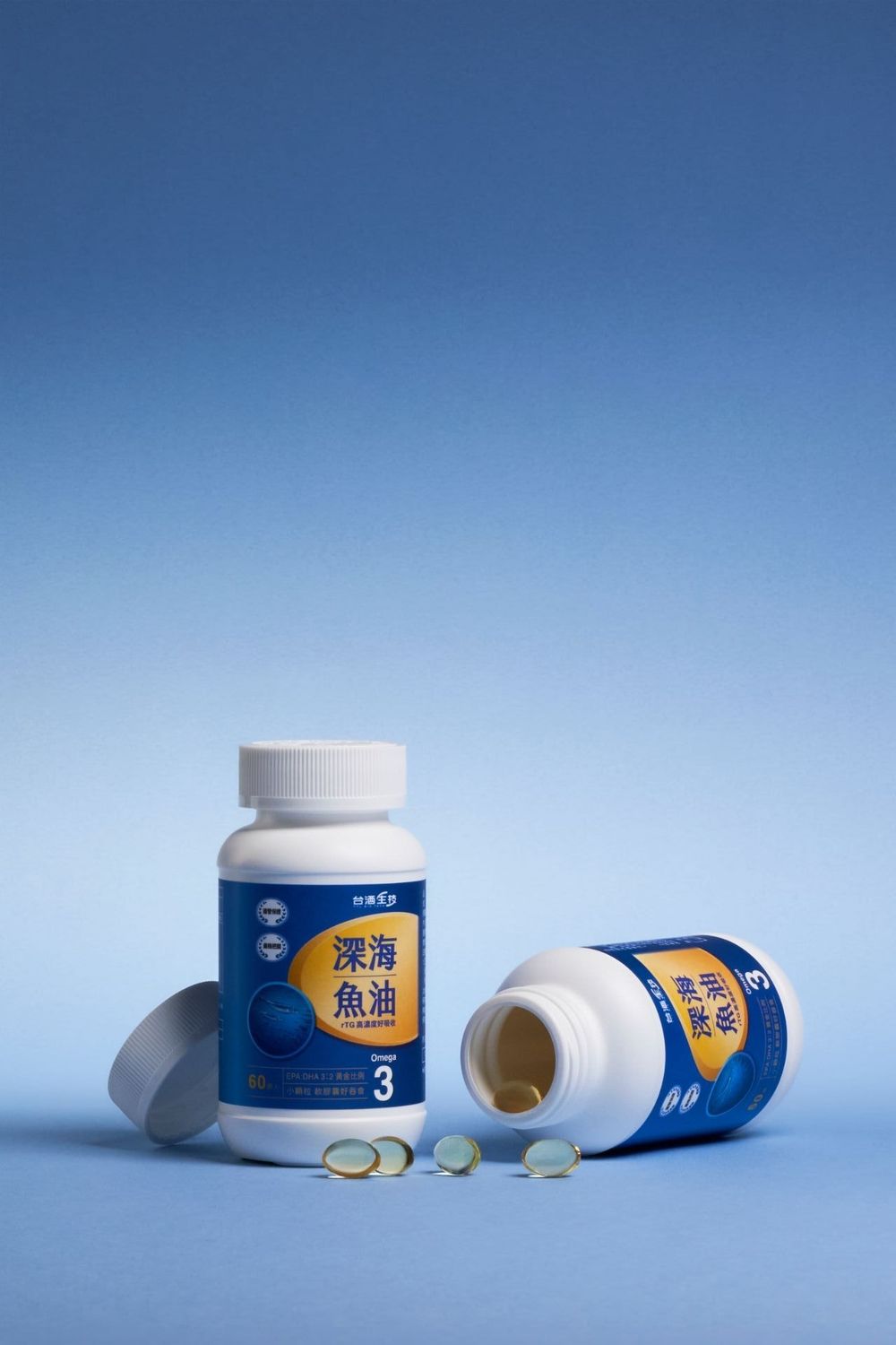 Two bottles of deep sea fish oil omega-3 supplements on blue background, one open with softgel capsules spilled out.