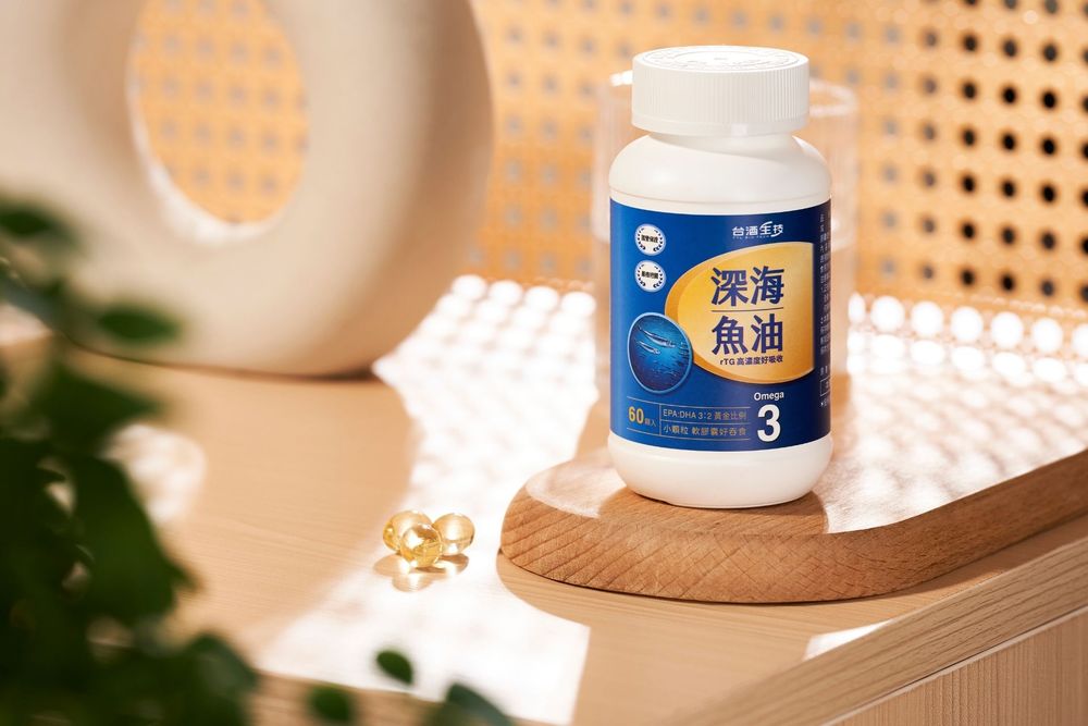 Deep sea fish oil omega-3 supplement bottle displayed on wooden tray with softgel capsule beside green plant.