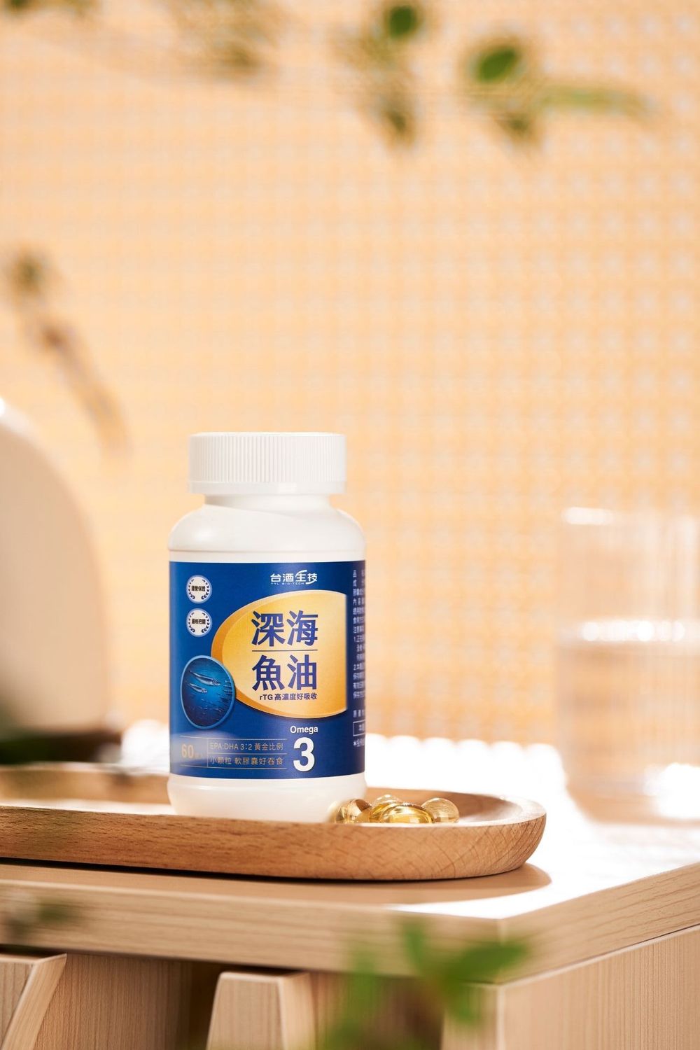 Deep sea fish oil Omega-3 supplement bottle displayed on wooden tray with golden capsules, glass of water, and green plants.