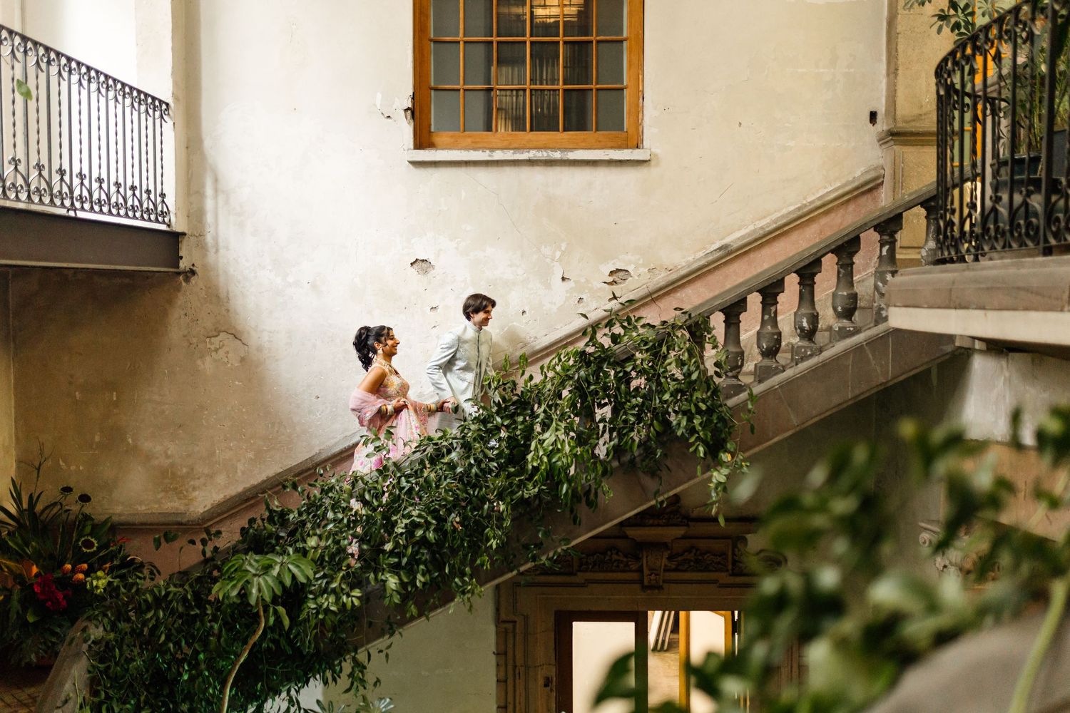 Couple in formal attire on a vine-covered stone staircase at an elegant European-style venue.