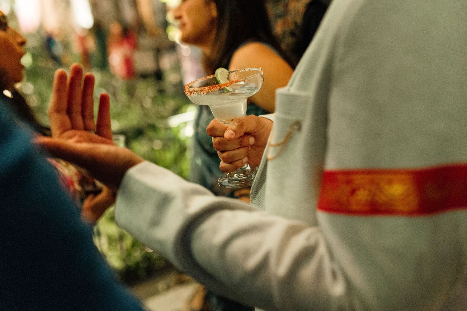 Person holding a elegant martini cocktail glass at a social gathering party event with blurred guests in background.