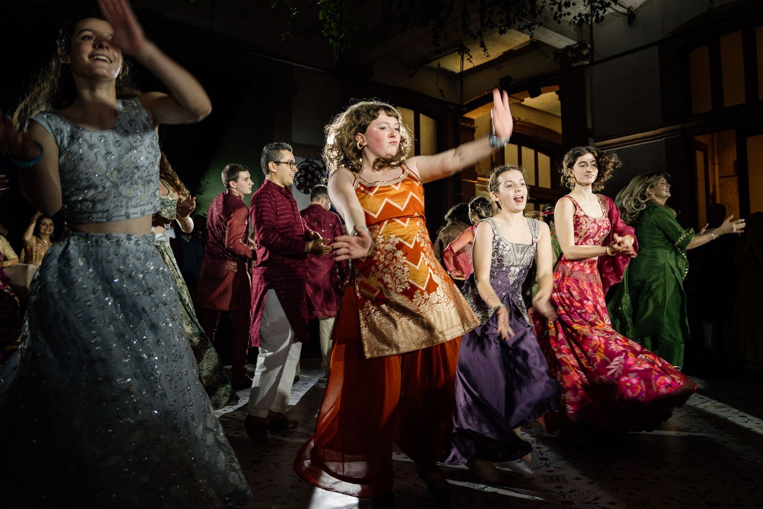 Young women in colorful traditional Indian gowns dance joyfully at an elegant evening celebration.