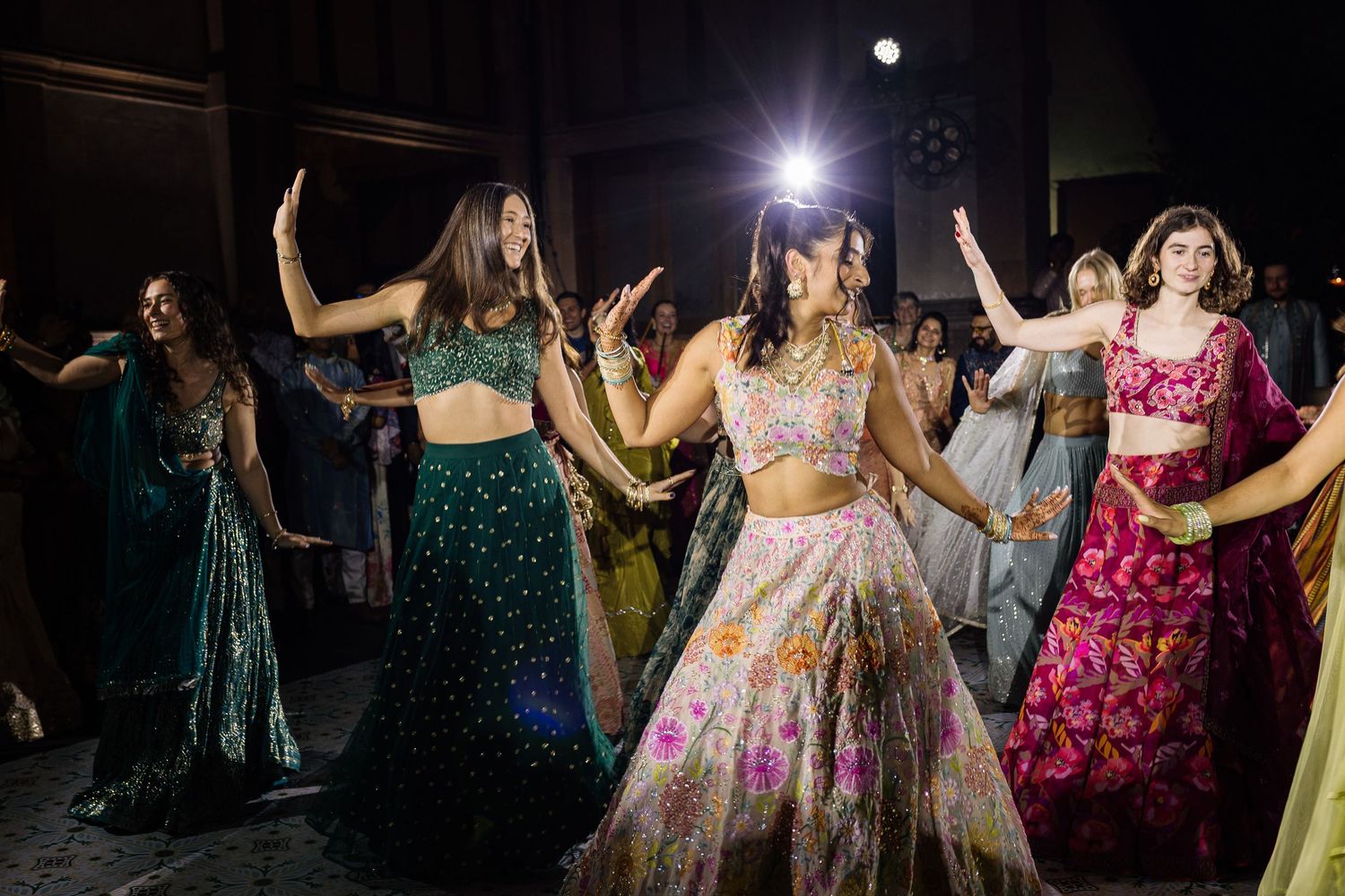 Women in colorful lehengas dancing joyfully at an Indian wedding celebration.
