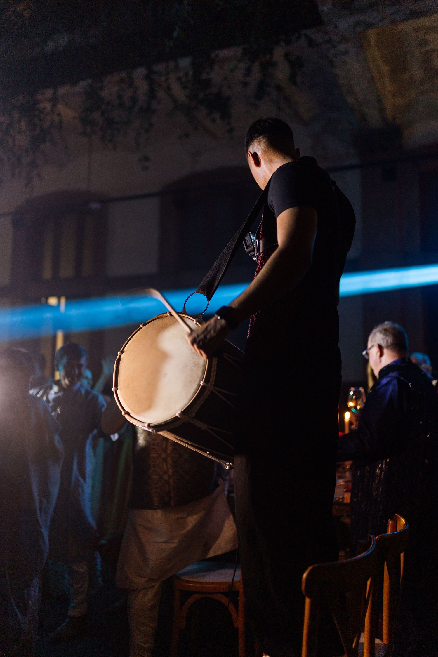 Musician playing a large drum on stage under blue lights at a live music event.