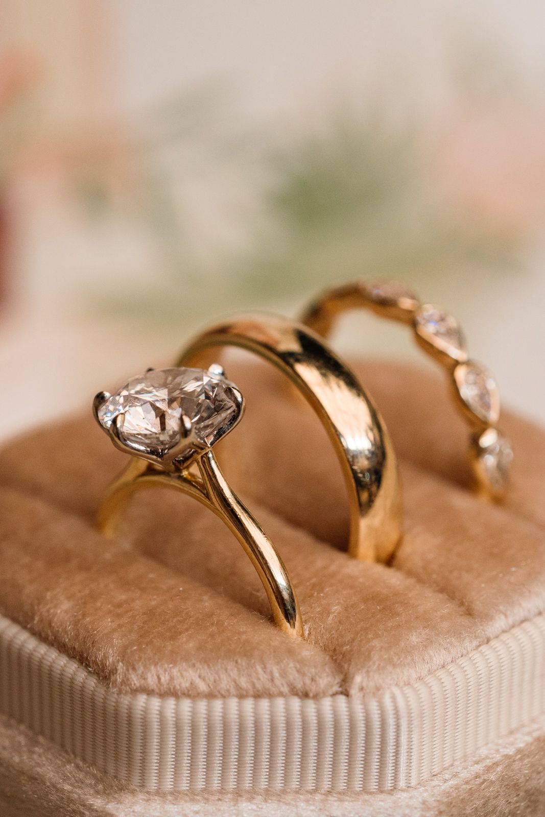 Three gold rings displayed in a velvet box, featuring a solitaire diamond engagement ring and two wedding bands.