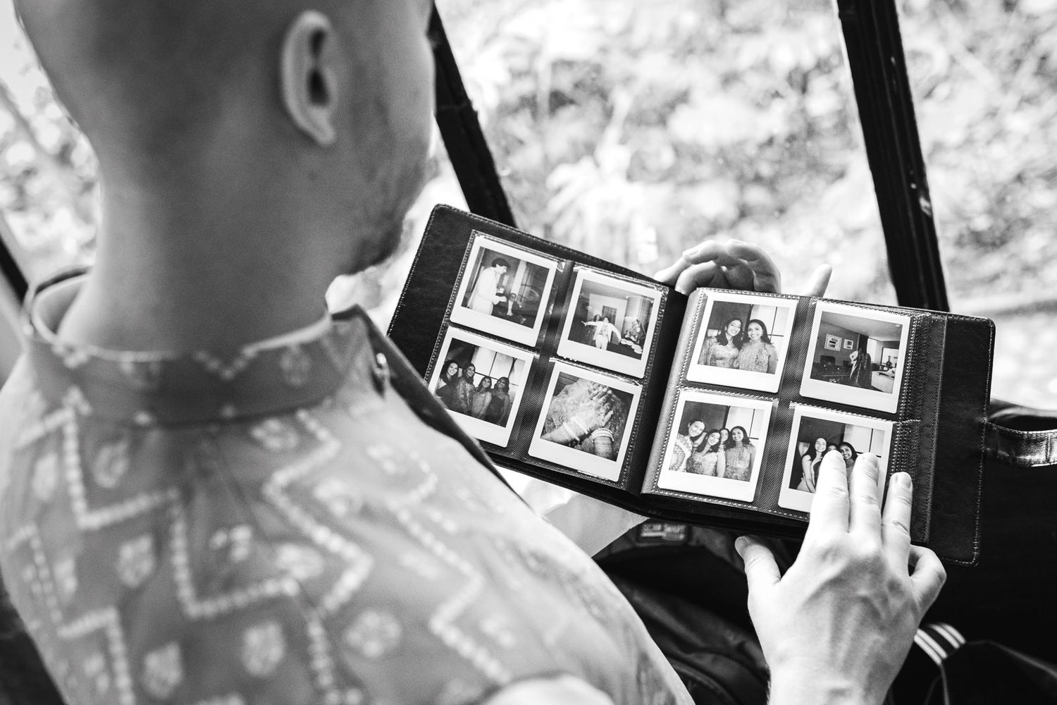 Groom reviews wedding photo album in black and white candid moment.