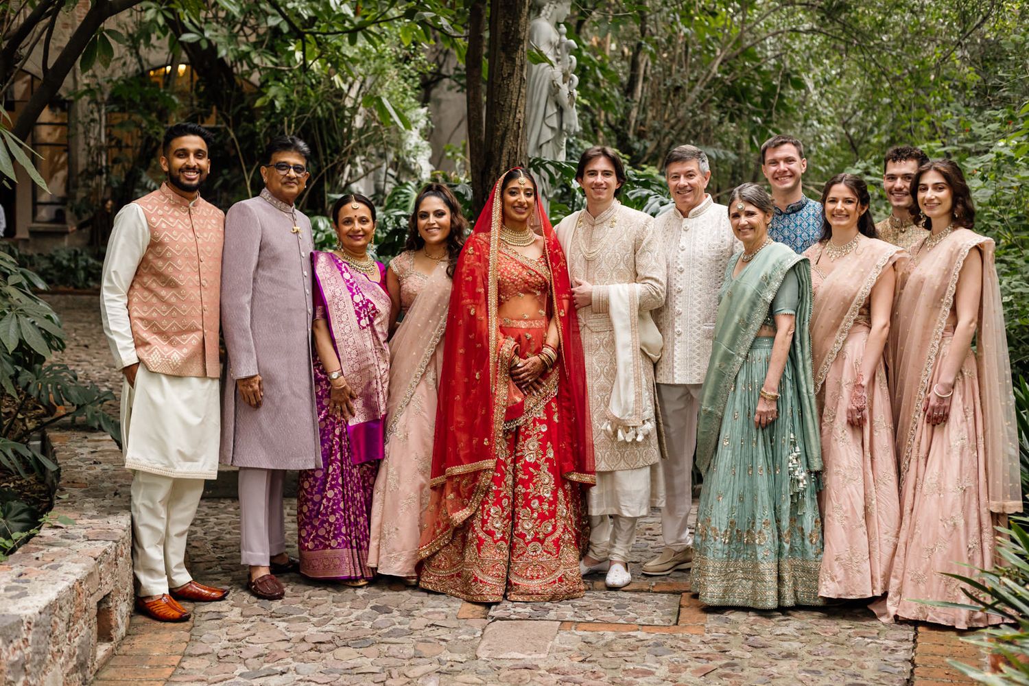 Group of elegantly dressed guests in traditional Indian attire posing together at a vibrant wedding celebration outdoors.