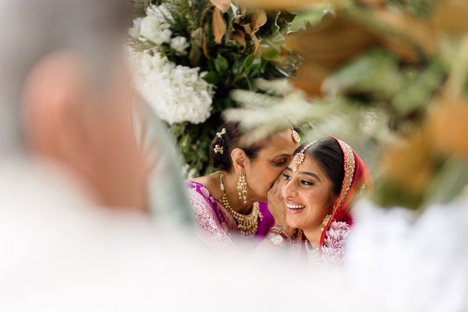 Bride and mother sharing a tender moment during an Indian wedding ceremony, adorned in vibrant traditional attire and jewelry.