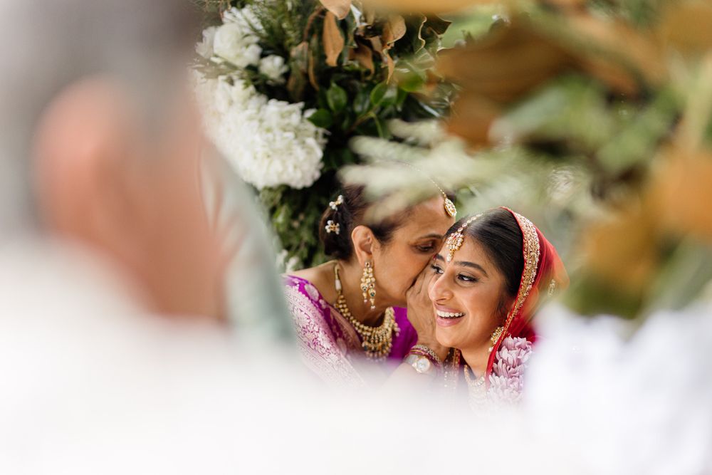 Bride and mother sharing a tender moment during an Indian wedding ceremony, adorned in vibrant traditional attire and jewelry.