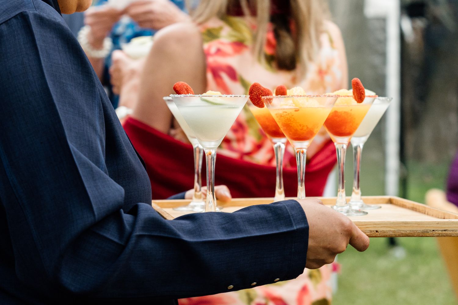 Waiter carrying a wooden tray with elegant martini glasses filled with strawberry and cream cocktails at an outdoor event.