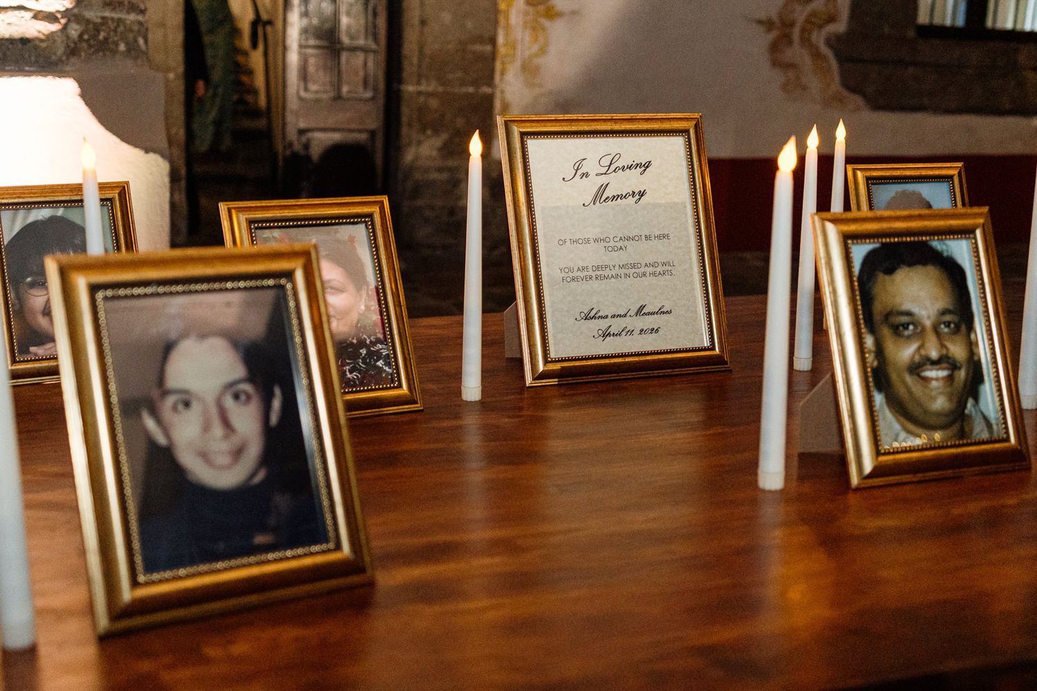 Memorial display with framed photos of deceased individuals, white candles, and an In Loving Memory card on a wooden table.