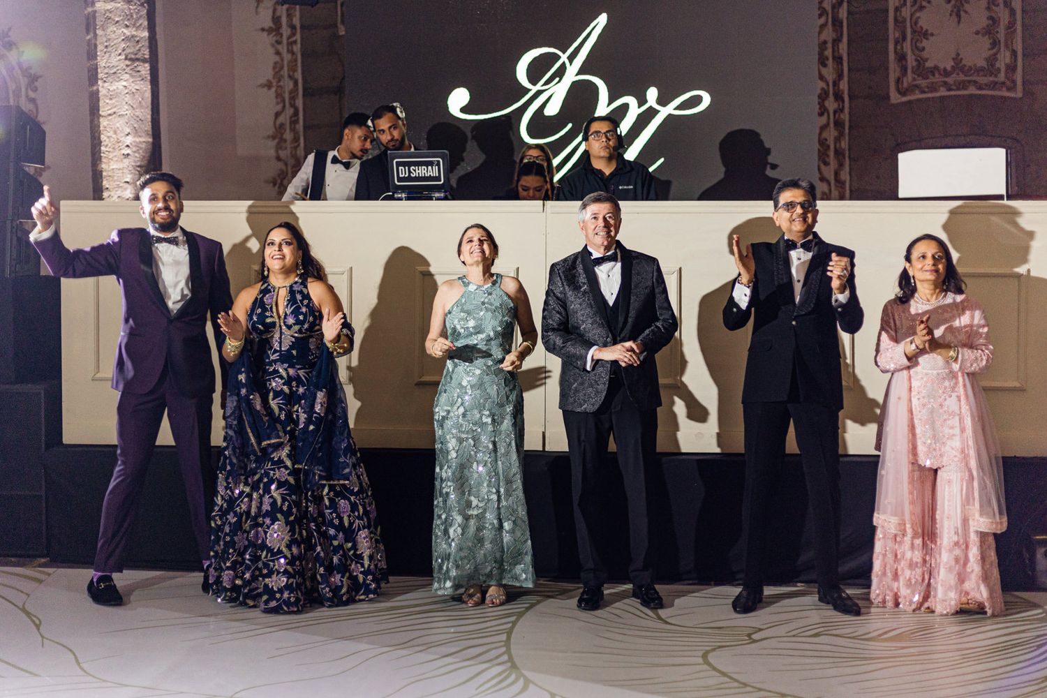 Elegantly dressed group posing at a formal event with decorative signage in a grand ballroom setting.