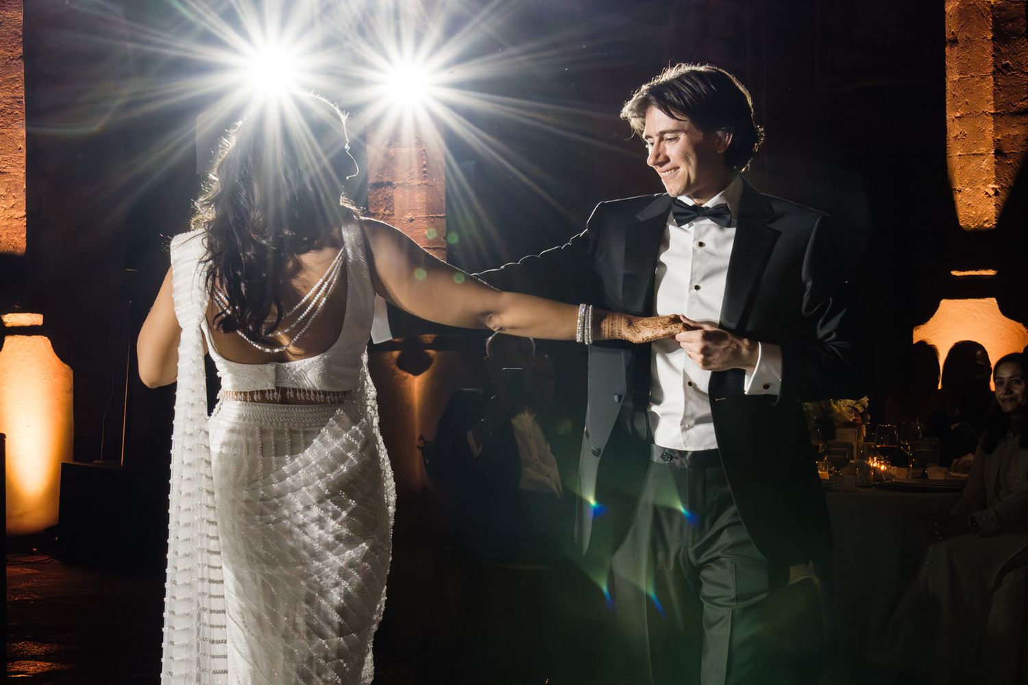 Bride and groom share their first dance at a romantic wedding reception with warm amber lighting.