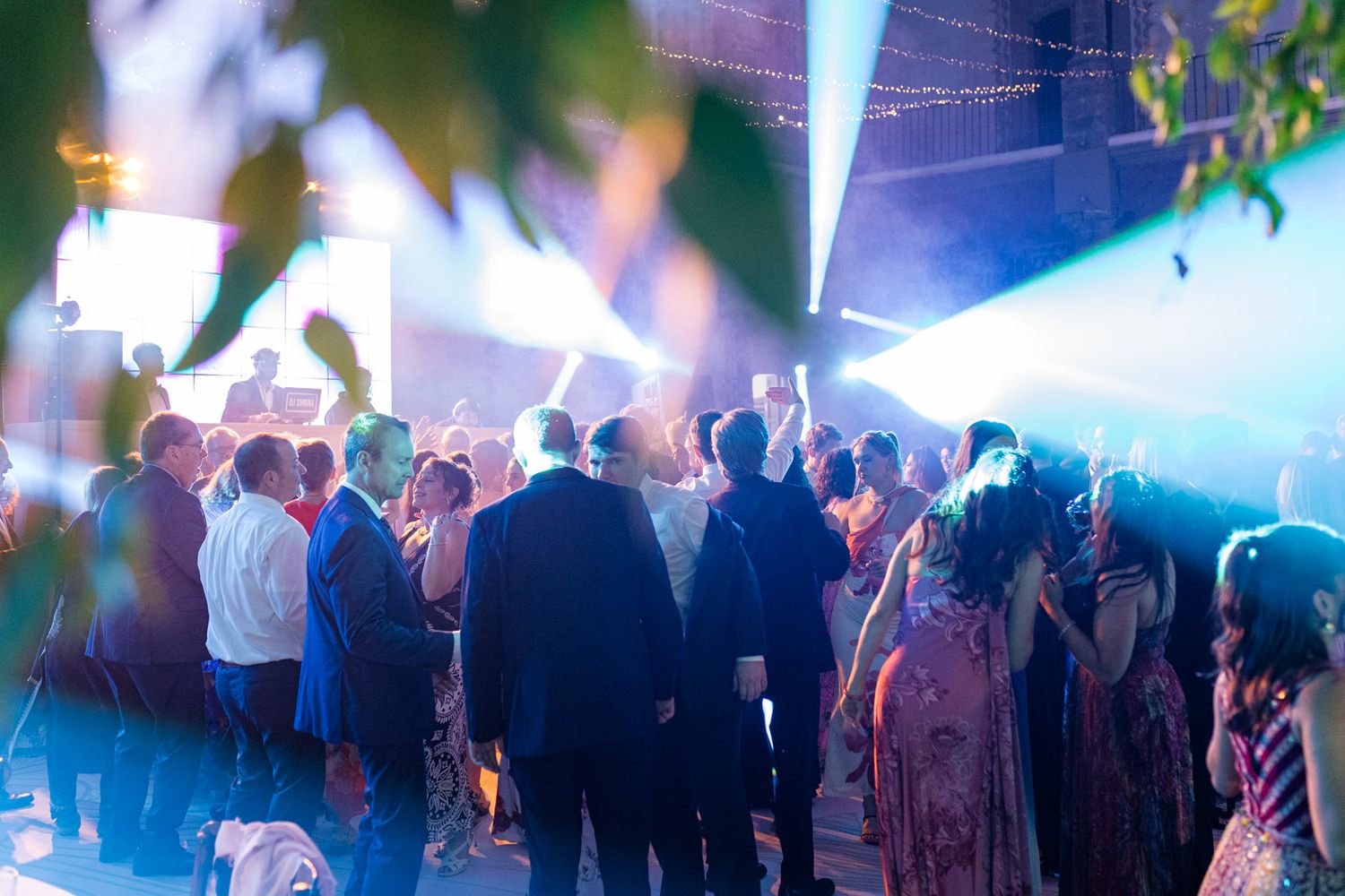 Crowd of guests dancing under blue stage lights at an outdoor evening wedding reception party.