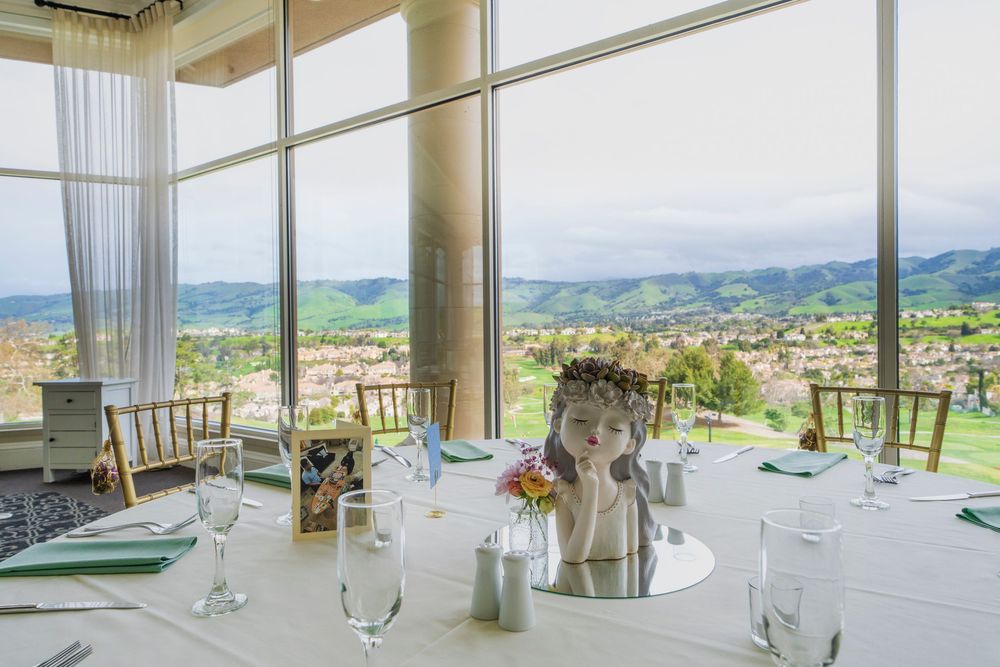 Elegant wedding reception venue with floor-to-ceiling windows overlooking rolling hills and a sculptural floral centerpiece.