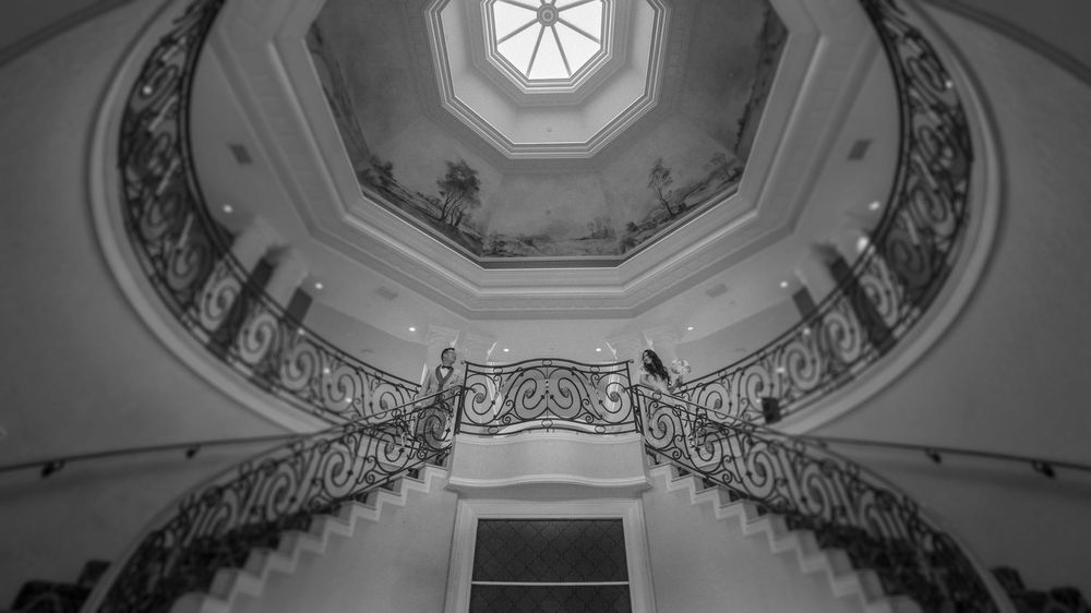 Black and white photo of an elegant spiral staircase with ornate railings beneath a domed skylight ceiling.