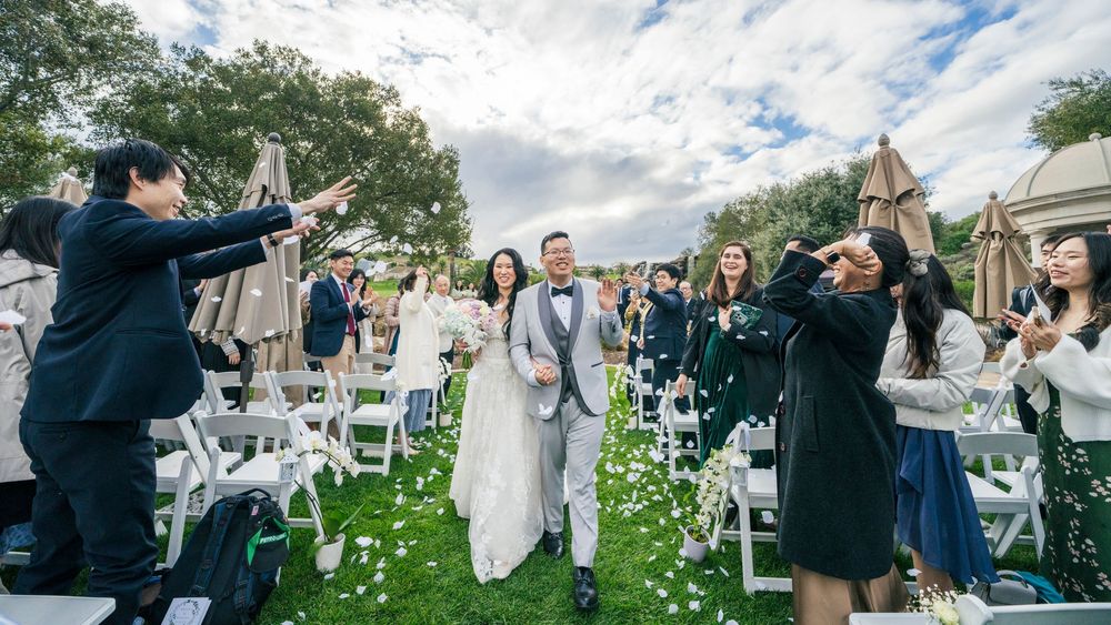 Joyful newlyweds walk down the aisle as guests toss confetti during an elegant outdoor wedding ceremony.
