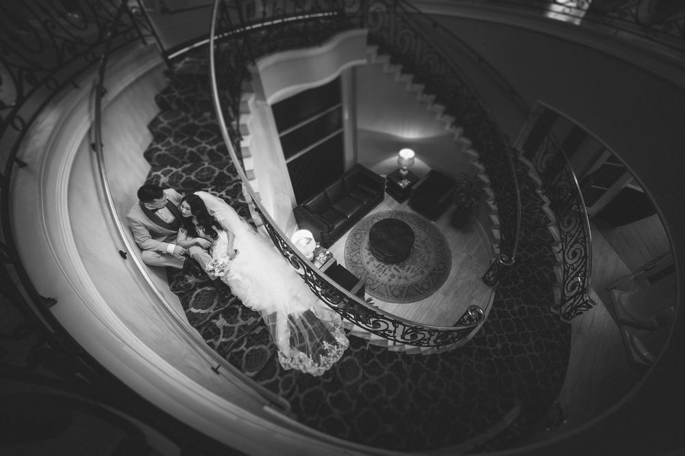 Aerial black and white photo of bride and groom on elegant spiral staircase with ornate railing.