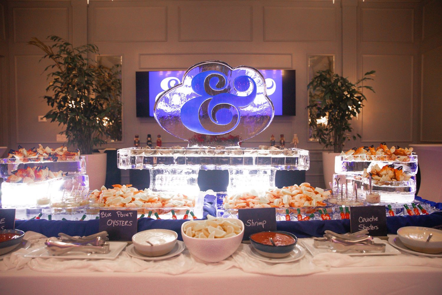 Elegant wedding buffet table with blue monogram backdrop, assorted appetizers, and decorative floral arrangements.