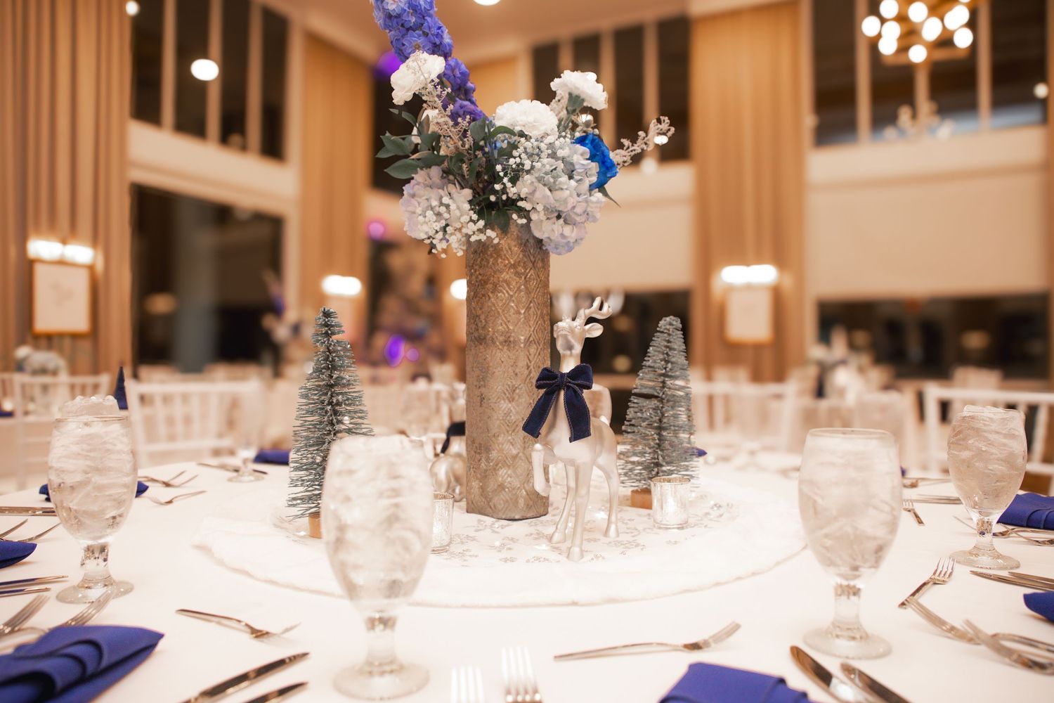 Elegant wedding reception table with blue napkins, crystal glasses, and a rustic wood centerpiece adorned with winter florals.
