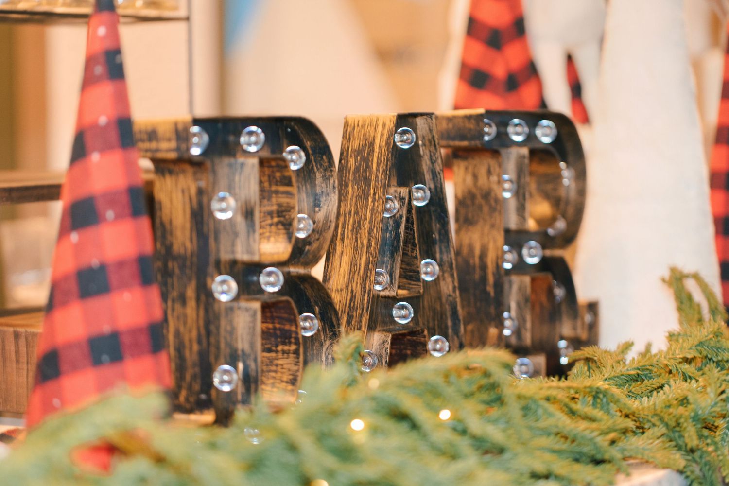 Rustic wooden BAR marquee sign with Edison bulbs, surrounded by plaid Christmas trees and greenery.