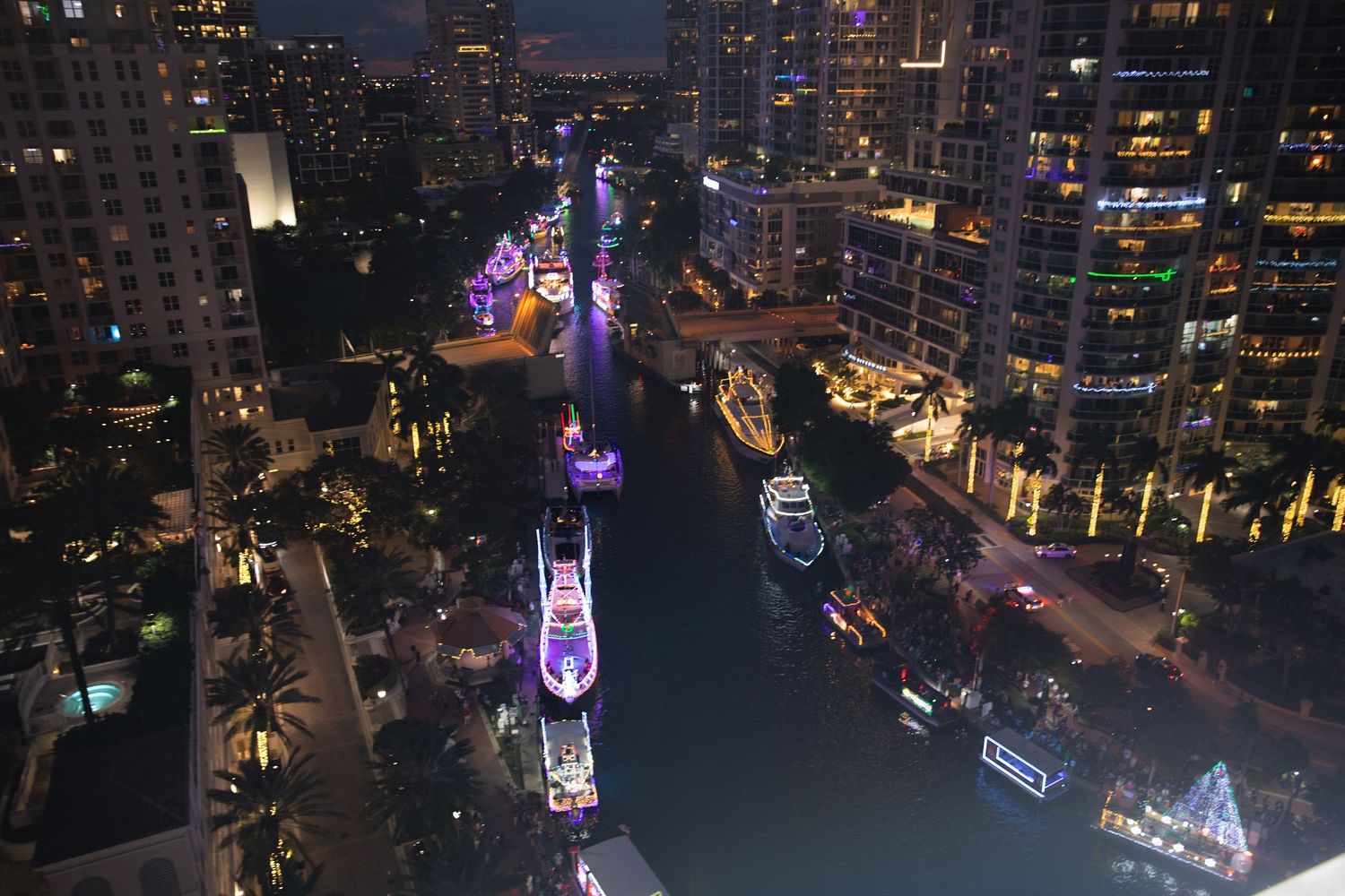 Aerial night view of a illuminated urban canal with luxury yachts and glowing city skyscrapers in Miami, Florida.